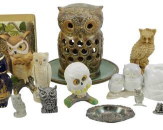 1254 - Assorted Owl Figures & Decorative Objects (Description): A collection of assorted owl figures and  decorative objects in various materials,  sizes, and styles. The grouping includes  ceramic, porcelain, glass, and metal owl  figurines, as well as a pierced ceramic owl candle holder or lantern, a small vase with  owl motif, a metal owl ashtray, and  decorative napkin holders or coasters  featuring owl imagery. The owls range from  naturalistic to whimsical in style, featuring