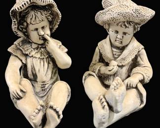 2002 - Pr Vintage Style Seated Children Statues 13" (Description): Pair of decorative statues depicting seated  children in vintage countryside attire. The  figures show a boy and girl, each wearing  wide-brimmed hats and period clothing,  rendered in an antiqued cream finish with dark accents highlighting the detailed  features. The charming figures are seated  cross-legged in relaxed poses. Measures 13  inches by 10 inches.