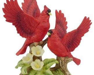 1089 - Johnathan Byron Ltd Ed Porcelain Cardinals (Description): Johnathan Byron limited edition porcelain  figurine featuring a pair of red cardinals  with wings spread, perched on naturalistic  tree branches. The base is adorned with  yellow primrose flowers and green foliage. The birds display characteristic cardinal  markings with black face masks and yellow  beaks. Measures 7 inches.