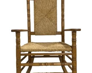 7637 - Porch Rocking Chair 45"x34"x26" (Description): The chair features a traditional design with  turned spindles on the arms and supports,  ball finials atop the back posts, and a  curved crest rail. Both the seat and back  panel are woven with rush in a radiating pattern. The chair includes a sturdy slatted  base with stretchers and curved rockers.  Measures 45" x 34" x 26".