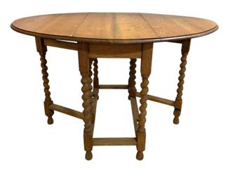 7759 - Oak Barley Twist Drop Leaf Gate Leg Table (Description): Vintage oak drop leaf table featuring  distinctive barley twist turned legs and a  gate leg design. The table has an oval top  when fully extended with two drop leaves  supported by swing-out gate legs. The piece includes stretcher supports between the legs  and rests on bun feet. Measures 29 inches  high by 47 inches wide by 35 inches deep when  open.