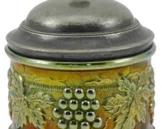 722 - Northwood Emerald Green Grape & Cable Powder (Description): Vintage Northwood Emerald Green Grape & Cable  Carnival Glass Powder Jar. This beautiful  piece features the classic grape and cable  pattern with raised grape clusters and  grapevine leaves encircling the body. The iridescent carnival glass displays rich  amber, green, and reddish tones with a  lustrous finish. The jar is topped with a  silver-toned metal lid featuring a decorative  acorn-style finial. A beaded rim accents the