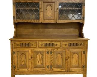 7764 - English Oak Gothic Revival Hutch w/ Leaded Glass (Description): 2-Piece Oak Gothic Revival style hutch  featuring upper display cabinet with leaded  glass doors in diamond lattice pattern  flanking a carved center panel with Gothic  arch motif. The lower buffet section has three drawers with slatted decorative details  above four cabinet doors with carved Gothic  arch panels. Features decorative metal hinges  throughout. Measures 64 inches wide by 60  inches tall by 17 inches deep.