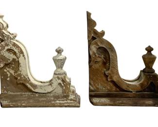7718 - Pr Antique Architectural Wood Corbels (Description): A pair of antique architectural wood corbels  featuring ornate scrollwork designs with  urn-shaped finials. One corbel retains  remnants of white paint with a weathered,  distressed patina, while the other displays natural aged wood tones. Both pieces show  authentic wear consistent with age and  salvage from a historic structure.  Measurements: 25" x 22" x 7".
