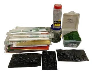 1696 - Assorted Model Railroad Scenery Supplies (Description): Assorted model railroad and diorama scenery  supplies including Woodland Scenics medium  ballast, green turf/grass material in  containers, various styrene and brass  modeling strips and rods in packaging, colored mesh sheets in gold, red, and green,  and several black plastic rock molds for  creating terrain features. Ideal for model  train layouts and miniature landscape  building.