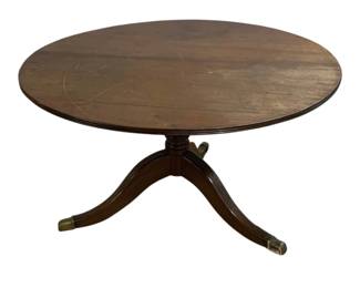 7587 - Antique Tilt Top Dining Table 26"x46" (Description): Round table featuring a mahogany finish with  a pedestal base supported by three splayed  legs with brass cap feet. The table has a  reeded column and classic Regency-style  design. Shows wear and surface scratches consistent with age. Measures 26 inches high  by 46 inches in diameter. Some wear and chips  in wood.