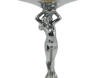 848 - Farber Bros Chrome Nude Compote (Description): Vintage Farber Bros. Art Deco compote  featuring a chrome-plated figural nude woman  stem supporting a Cambridge amber glass bowl  with scalloped chrome overlay rim. The  elegant female figure stands on a round chrome base with arms raised to hold the bowl  aloft. Measures 8 inches tall by 5 inches in  diameter.