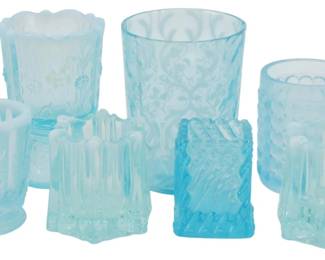 765 - Assorted Blue Opalescent Pressed Glass (Description): A collection of assorted blue opalescent  pressed glass pieces featuring various  decorative patterns. The grouping includes  tumblers, toothpick holders, and small  vessels in pale blue glass with characteristic opalescent white edges and  rims. Each piece displays intricate pressed  designs including floral motifs, geometric  patterns, and textured surfaces typical of  Victorian-era American pressed glass.
