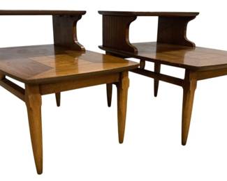 7603 - Pair Lane #1927 MCM Two-Tier End Tables (Description): Pair of mid-century two-tier end tables  featuring parquet-style wood veneer tops with  a warm walnut finish. Each table has a  stepped upper shelf supported by curved  supports and sits on four tapered legs in a lighter oak tone. The two-tier design is  characteristic of the mid-century modern era,  offering both style and functionality.  Measures 22" x 30" x 20".