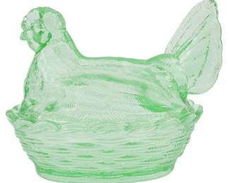 1045 - Green Glass Hen on Nest Figure 5"x6"x4.5" (Description): A charming green glass hen on nest figure,  crafted in translucent pressed glass with a  soft, pale green hue. The hen sits atop a  decorative woven basket-style base, with  detailed feather texturing visible throughout the body, wings, and tail. This classic  covered dish design features a removable hen  lid. Measures 5" x 6" x 4.5".