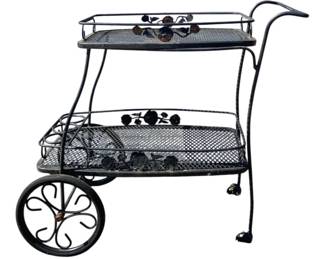 7690 - Two-Tier Metal Outdoor Teacart (Description): Two-tier outdoor teacart featuring mesh  shelving and decorative floral accents. The  cart has a black finish with scrollwork wheel  design and a curved push handle. Note:  missing wheels. Measures 32" x 40" x 21".