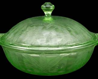 889 - Jeanette Poinsettia Uranium Glass Casserole (Description): Vintage Jeanette Poinsettia pattern uranium  glass covered casserole dish in green.  Features the distinctive pressed floral and  leaf design characteristic of this  Depression-era pattern, with a domed lid topped by a faceted finial and tab handles on  each side. Measures 5.5" x 10.5".