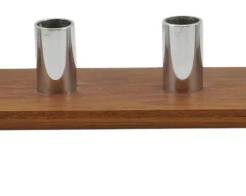 970 - Mid Century Teak & Chrome Candlestand 3.5x20" (Description): Mid Century candlestand featuring a sleek  teak wood base mounted on two chrome pedestal  feet. The piece holds six polished chrome  cylindrical candle cups arranged in a single  row along the top. A striking example of mid-century modern design combining warm wood  tones with cool metallic accents. Measures 3  1/2" x 20" x 3".
