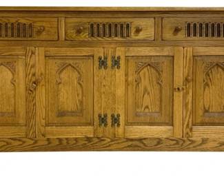 7780 - Oak Gothic Revival Style Buffet Sideboard (Description): Oak buffet sideboard in Gothic Revival style  featuring four doors with carved pointed arch  panels and decorative iron butterfly hinges.  The upper section has three drawers with  round wooden knobs and slatted ventilation panels. The piece rests on square legs and  displays a warm honey-toned finish. Measures  32" high x 60" wide x 17" deep.