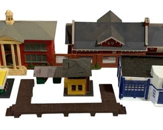1708 - Lot HO Scale Model Railroad Buildings (Description): A collection of HO scale model railroad  buildings including a red brick schoolhouse  or municipal building with columned entrance  and cupola, a large train depot or station  with gray roof, a Coca-Cola billboard stand, a small yellow station building,a blue and  white industrial or commercial structure, and  brown platform sections. Ideal for model  railroad layouts and dioramas.