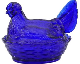 1044 - Cobalt Glass Hen on Nest Figure 5"x6"x4.5" (Description): Cobalt glass hen on nest figure in a rich,  deep blue color. The decorative covered dish  features a detailed hen sitting atop a woven  basket-style base. The pressed glass  construction showcases intricate feather texturing on the hen and a basketweave  pattern on the nest. Measures 5" x 6" x 4.5".
