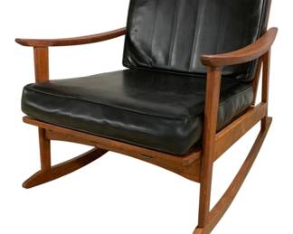 7630 - Mid-Century Modern Teak Rocker att. Moreddi (Description): Mid-Century Modern Danish rocking chair  attributed to Moreddi featuring a teak wood  frame with sculptural curved arms and  rockers. The chair has black cushions for  both the seat and back. The clean lines and warm wood tones are characteristic of the  mid-century aesthetic. Measures 28 inches  wide by 27 inches deep by 32 inches tall.