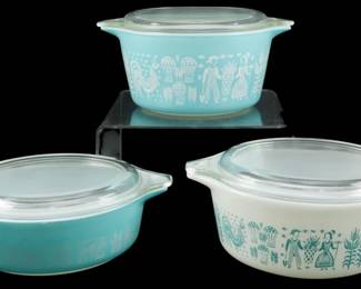 1040 - 4Pc Pyrex Butterprint Casserole Set (Description): Four-piece Pyrex Butterprint casserole set  featuring the iconic Amish pattern with  turquoise and white colorways. The set  includes three casserole dishes with clear  glass lids, showcasing the distinctive folk art design of roosters, corn, and Amish  figures. Two dishes feature turquoise  backgrounds with white pattern details, while  one displays the reverse colorway with white  background and turquoise pattern. Each