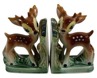 1548 - 2pc Vtg Ceramic Deer Fawn Bookends Set (Description): A charming pair of vintage ceramic deer  bookends featuring spotted fawns posed beside  tree stumps. The bookends are finished in  warm brown tones with white spotted detailing  on the fawns' backs, cream-colored faces, and green grassy bases. Each bookend measures   7" x 4" x 5".