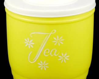 1195 - Stanley Tea Canister in Yellow 5"x5" (Description): Stanley Tea Canister in yellow with white  lid. This charming vintage-style canister  features the word "Tea" in elegant white  script, surrounded by decorative white daisy  motifs. The canister has a round form with a fitted lid featuring a flip-top oening.  Measures 5" x 5".