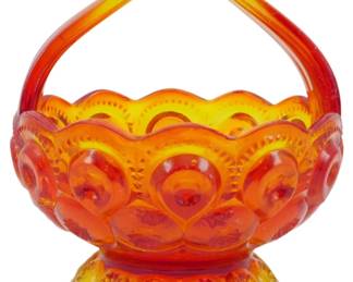 999 - Vtg L.E. Smith Amberina Moon & Stars Basket (Description): Vintage L.E. Smith Amberina Moon & Stars  pattern glass basket. This striking piece  features the classic Moon & Stars motif with  circular medallions and teardrop designs  throughout the bowl. The amberina coloring transitions beautifully from deep red at the  base through vibrant orange to golden yellow  at the scalloped rim and arched handle. The  footed base displays a matching decorative  pattern. Measures 5 inches by 4.5 inches.