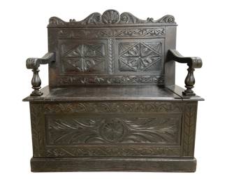 7751 - Heavily Carved Oak Hall Bench w/ Storage (Description): Antique carved oak hall bench with storage  compartment beneath the hinged seat. This  handsome piece features elaborate carved  details throughout, including geometric  rosette panels on the high back, a decorative shell-form crest rail, scrolling acanthus  leaf motifs on the front panel, and turned  baluster arm supports. The dark oak finish  has developed a rich patina. Measures 42"  high x 42" wide x 23" deep.