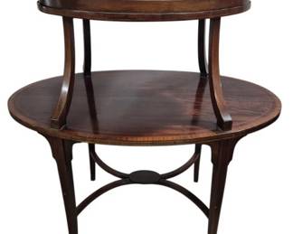 7757 - 19th C English 2 Tier Tea Table w/ Tray (Description): Antique mahogany two-tier oval table  featuring elegant curved supports connecting  the upper and lower tiers. The table stands  on four gracefully tapered legs joined by a  curved stretcher base with a central medallion detail. Adorned with original  fitted oval framed glass tray with tall  curved brass handles. The warm brown finish  highlights the fine wood grain throughout.  Measures 36 inches by 36 inches by 22 inches.
