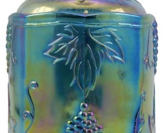 679 - Indiana Harvest Grape Blue Carnival Jar (Description): Vintage Indiana Harvest Grape electric blue  carnival glass canister jar. This covered jar  features the classic grape and leaf pattern  in relief, with a grape cluster finial on the  lid. The iridescent blue carnival glass displays the characteristic rainbow sheen  that shifts between blue, purple, green, and  gold tones. Measures 7 inches tall by 4  inches in diameter.