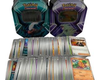 1566 - Lot of 200 Pokemon Cards w/ 2 Tins (Description): Lot of 200 Pokemon trading cards accompanied  by two official Pokemon Trading Card Game  collector tins. The tins feature distinctive  hexagonal designs with viewing windows on the  lids. The card collection includes various types with holographic and standard cards  visible among the assortment.