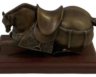 1530 - Bronze Horse Statue on Wood Base 8"x5"x6" (Description): Bronze horse statue depicting a recumbent  saddled horse in a Tang dynasty style. The  horse is shown kneeling with legs tucked  beneath its body, wearing an ornate saddle  blanket with decorative scrollwork patterns. The figure displays fine detailing including  a clipped mane and braided tail. Mounted on a  dark wood rectangular base. Measures 8" x 5"  x 6".