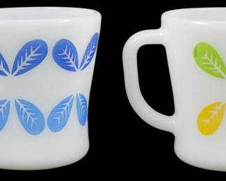 1114 - Pr Vtg Federal Leaf 2 Color Mugs 3.5" (Description): Pair of vintage Federal Glass leaf pattern  mugs measuring 3.5 inches. These milk glass  mugs feature a distinctive two-tone leaf  design in rows of two. One mug displays the  pattern in shades of blue, while the other showcases green and yellow leaves.Each leaf  motif includes a white feather or fern detail  within. Classic mid-century American  glassware with the characteristic D-handle  design.