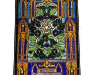 7627 - Gothic Style Stained Glass Panel 35"x21" (Description): A striking Gothic style stained glass panel  featuring an ornate central floral medallion  with dark flowers and green foliage. The  design incorporates architectural elements  including pointed Gothic arch motifs in amber and gold tones, set against vibrant cobalt  blue and turquoise glass. Decorative  fleur-de-lis accents appear at the top, while  the lower portion features lavender and  purple glass in a geometric arrangement. The