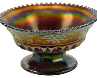 729 - Northwood Amethyst Grape & Cable Candy Bowl (Description): Vintage Northwood amethyst Grape & Cable  pattern carnival glass candy bowl. This  footed compote-style bowl features the  classic pressed grape and cable design with a  beaded rim edge. The iridescent finish displays rich purple, gold, and multicolored  rainbow hues characteristic of fine carnival  glass. Measures 3 inches tall by 5 inches in  diameter.