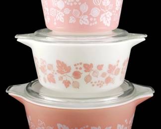 1196 - 3pc Pyrex Pink Gooseberry Casserole Set (Description): Three-piece Pyrex Pink Gooseberry casserole  set featuring the classic mid-century pattern  with gooseberries, leaves, and small  flowers. The set includes three graduated  sizes with matching clear glass lids. Two dishes feature pink bodies with  whitedecoration, while one has a white body  with pink decoration, creating the desirable  complementary color scheme. Measures 4 inches  by 11 inches by 8 inches.