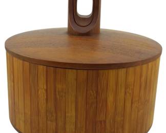 980 - Jens Quistgaard Dansk Teak Ice Bucket (Description): Mid Century Dansk Denmark teak ice bucket  featuring a cylindrical body with vertical  slat construction and a fitted lid topped  with a sculptural carved teak handle with an  open loop design. The warm honey-toned wood showcases the characteristic Danish modern  aesthetic. Measures 10 inches by 10 inches.