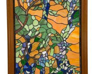 1506 - Stained Glass Window Wisteria 36.5x22.5 (Description): A stained glass window featuring a wisteria  design with cascading blue and purple  blossoms amid green foliage against a warm  amber and orange background. The intricate  leaded glass panel displays brown branches winding throughout the composition in a  Tiffany-inspired style. Presented in a wooden  frame. Measures 36 1/2 inches by 22.5  inches.