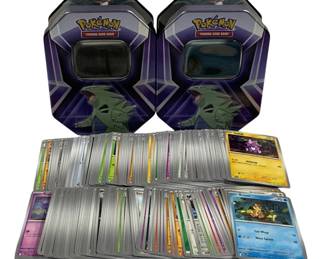 1565 - Lot of 200 Pokemon Cards w/ 2 Tyranitar Tins (Description): A collection of 200 Pokemon trading cards  accompanied by two matching Tyranitar  collector tins. The cards include a variety  of types and characters from different  Pokemon TCG sets, featuring both common and holographic cards. The purple and silver  hexagonal tins feature Tyranitar artwork and  include viewing windows on top. An excellent  lot for collectors or players looking to  expand their Pokemon card collection.