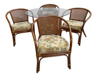 7679 - Bamboo & Rattan Glass Top Table w/ 4 Chairs (Description): Bamboo and rattan dining set featuring a  round glass top table and four matching  chairs. The chairs feature cane backs and  floral upholstered cushion seats in cream  with pink, green, and blue botanical designs. The warm honey-toned bamboo frames have  curved arms and decorative wrapped joints.  Table measures 24" x 42" does hav chips on  edges, chairs measure 31" x 23" x 25".