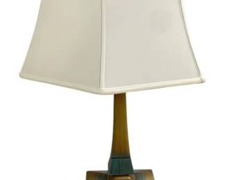 7634 - Mid-Century Verdigris Decorated Table Lamp (Description): Featuring a brass-toned body with verdigris  patina accents. The lamp has a tiered,  architectural base with squared pedestal  sections leading to a tapered column. Topped  with a square white fabric shade and decorative brass finial. The lamp exhibits a  sophisticated, mid-century aesthetic with its  combination of warm brass tones and aged  green patina detailing. Used as is electric/electronic/mechanical