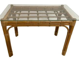 7657 - Bamboo Glass Top Table 23"x33"x19" (Description): Bamboo glass top table featuring a  rectangular beveled glass surface resting on  a natural bamboo frame. The table showcases  traditional rattan-wrapped joints at the  corners and along the legs, with curved bamboo supports connecting the legs to the  apron. The warm honey-toned bamboo finish  gives this piece a classic tropical or  bohemian aesthetic. Measures 23 inches wide  by 33 inches long by 19 inches high.