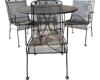 7694 - Metal Patio Table & 4 Chairs (Description): Vintage outdoor table and chair set featuring  a round mesh-top table with four matching  armchairs. The set displays decorative  scrollwork and grape leaf motifs along the  chair backs, characteristic of mid-century patio furniture design. The black iron  construction features expanded metal mesh  seats and backs. Measures 29 inches by 48  inches, with chairs measuring 36.5 inches by  21 inches by 24 inches.