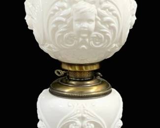 1653 - Gone with the Wind Lamp w/ Cherub Motif 30" (Description): Gone with the Wind style parlor lamp  featuring white milk glass globe shade and  font, both decorated with raised cherub face  and scrolling acanthus leaf motifs. The lamp  sits on an ornate cast metal base with a brass-tone finish. Fitted with a brass  collar, chimney holder, and clear glass  chimney. Measures 30 inches tall. Used as is electric/electronic/mechanical  item. No guarantee all components, untested.