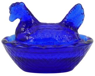 1053 - Cobalt Glass Miniature Hen on Nest Figure (Description): Cobalt glass miniature hen on nest figure.  This charming decorative piece features a  detailed hen lid resting atop a basket-weave  patterned nest base. The deep cobalt blue  glass showcases rich color saturation with textured feather details on the hen portion.  Measures 2 inches by 2.5 inches by 2 inches.