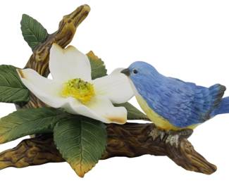 1080 - Andrea by Sadek Porcelain Bluebird Figure (Description): Andrea by Sadek porcelain bird figure  depicting a bluebird perched on a  naturalistic branch with a white dogwood  blossom and green leaves. The bird is  hand-painted in vibrant blue with a yellow breast. Measures 4.5 inches.