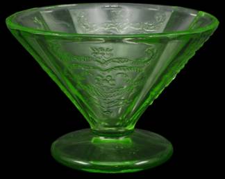 891 - Vtg Federal Madrid Uranium Glass Sherbet (Description): Vintage Federal Madrid pattern uranium glass  sherbet dish in a distinctive green color.  This Depression-era piece features the  characteristic embossed floral and swag  design typical of the Madrid pattern, with a footed base and cone-shaped bowl. The glass  exhibits the characteristic uranium green  glow associated with vaseline glass from this  period. Measures 3 inches tall by 4 inches  in diameter.