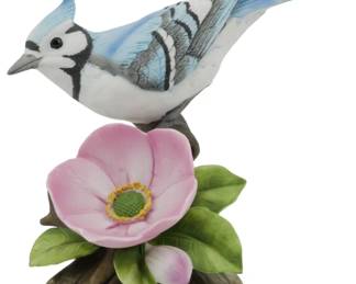 1074 - Andrea by Sadek Blue Jay Porcelain Figure 5" (Description): Andrea by Sadek porcelain figurine depicting  a blue jay perched on a branch with a pink  wild rose bloom and green leaves. The bird  features hand-painted details in shades of  blue, white, black, and gray, capturing the distinctive crest and markingsof the species.  Measures 5 inches.