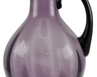782 - Blenko Amethyst Art Glass Pitcher 13" (Description): Blenko amethyst art glass pitcher featuring  an elegant baluster form with an elongated  pointed spout and contrasting dark applied  handle. The deep purple glass body displays  beautiful translucency with subtle optic ribbing. Measures 13 inches tall.