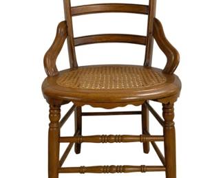 7667 - Victorian Walnut Cane Seat Chair (Description): Featuring a ladder back design with  decorative carved crest rail. The chair has  gracefully curved arms and turned front legs  with stretcher supports. The oval seat is  woven cane in good condition. The chair displays a warm honey-toned wood finish.  Measures 34"x18"x18".