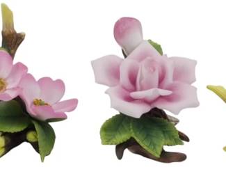 1091 - 4 Assorted Makers Porcelain Flowers (Description): A collection of four porcelain flowers from  assorted makers. The grouping includes three  pink rose arrangements featuring blooms and  buds on naturalistic branch bases with green  leaves, and one pale cream-colored flower on a driftwood-style base. Each piece is  delicately hand-painted with realistic  coloring and details.