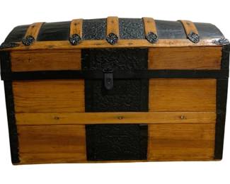 7720 - Vtg Dome Top Steamer Trunk w/ Metal Hardware (Description): Vintage dome top steamer trunk featuring  wooden slat construction with decorative  embossed metal banding and corner accents.  The trunk displays a warm honey-toned wood  finish contrasted with black metal trim and hardware. Decorative quatrefoil medallions  adorn the front, and a central metal latch  closure secures the lid. Has fitted interior  tray. The piece exemplifies late 19th to  early 20th century travel trunk styling with